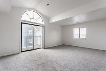 A spacious room with a large arched window and a sliding glass door leading to a balcony.